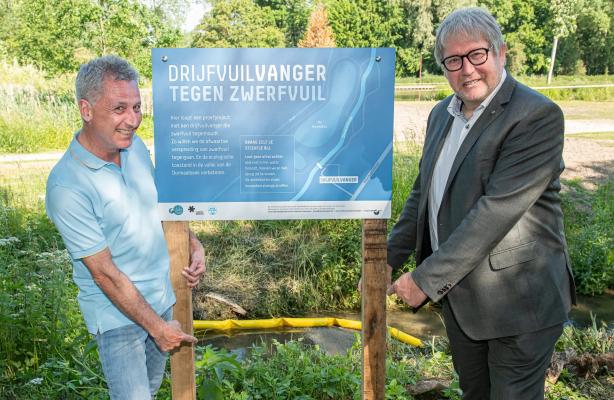 Gedeputeerde Bart Nevens en schepen Gary Peeters plaatsen het infobord aan de drijfvuilvanger in de Dormaalbeek in Landen